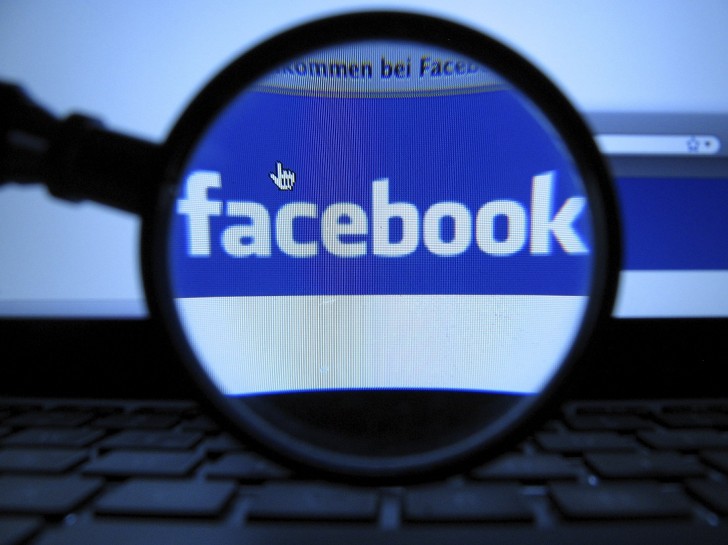 A magnifying glass is posed over a monitor displaying a Facebook page in Munich.